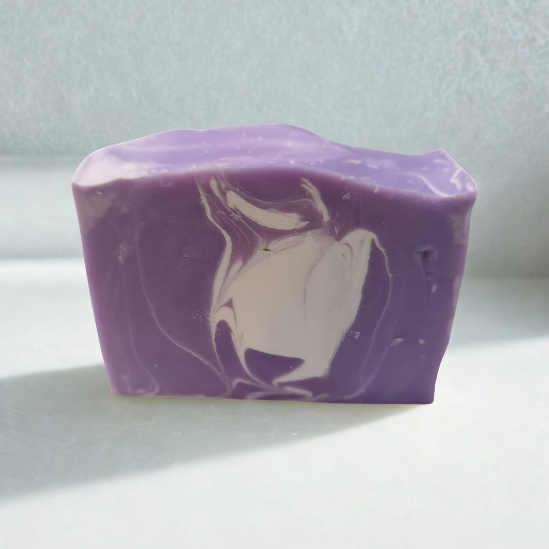 A rectangular bar of purple soap with a white marbled swirl pattern, photographed on a light gray surface with a textured light gray background.